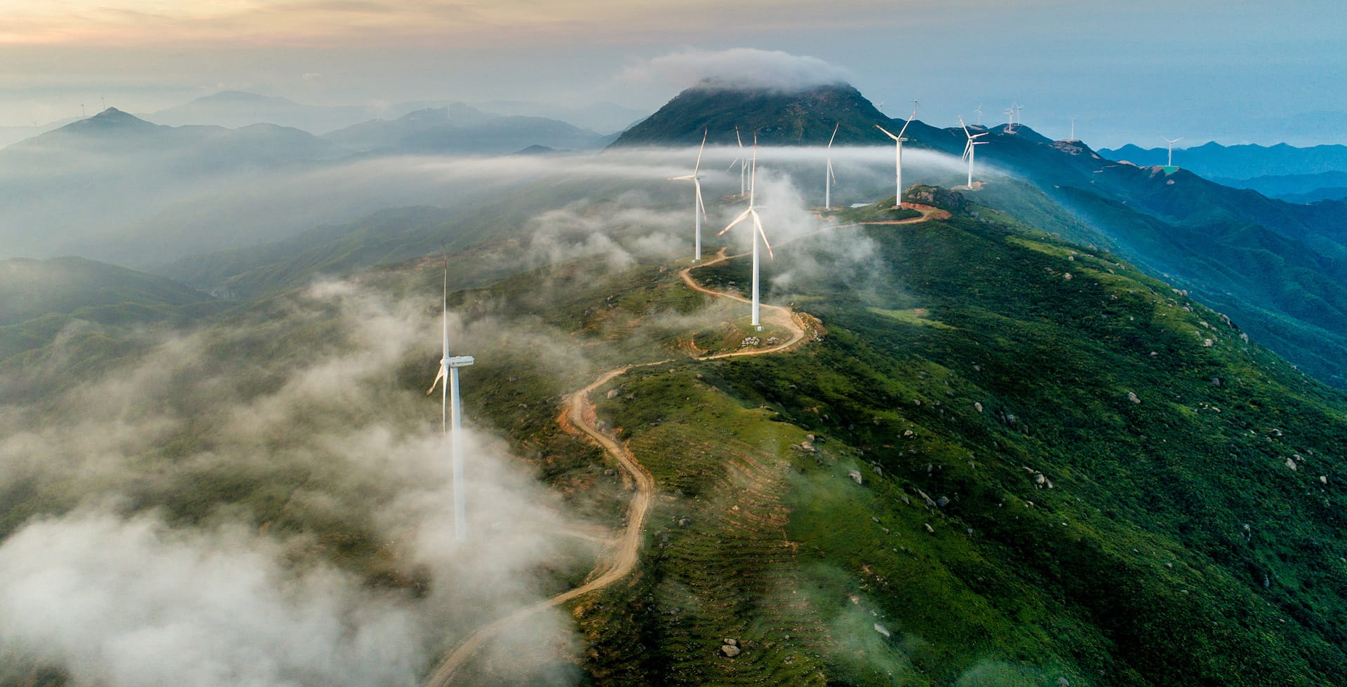 Parc éolien sur une montagne verte entourée de brume - Comment les obligations vertes peuvent favoriser la transition vers un avenir plus durable