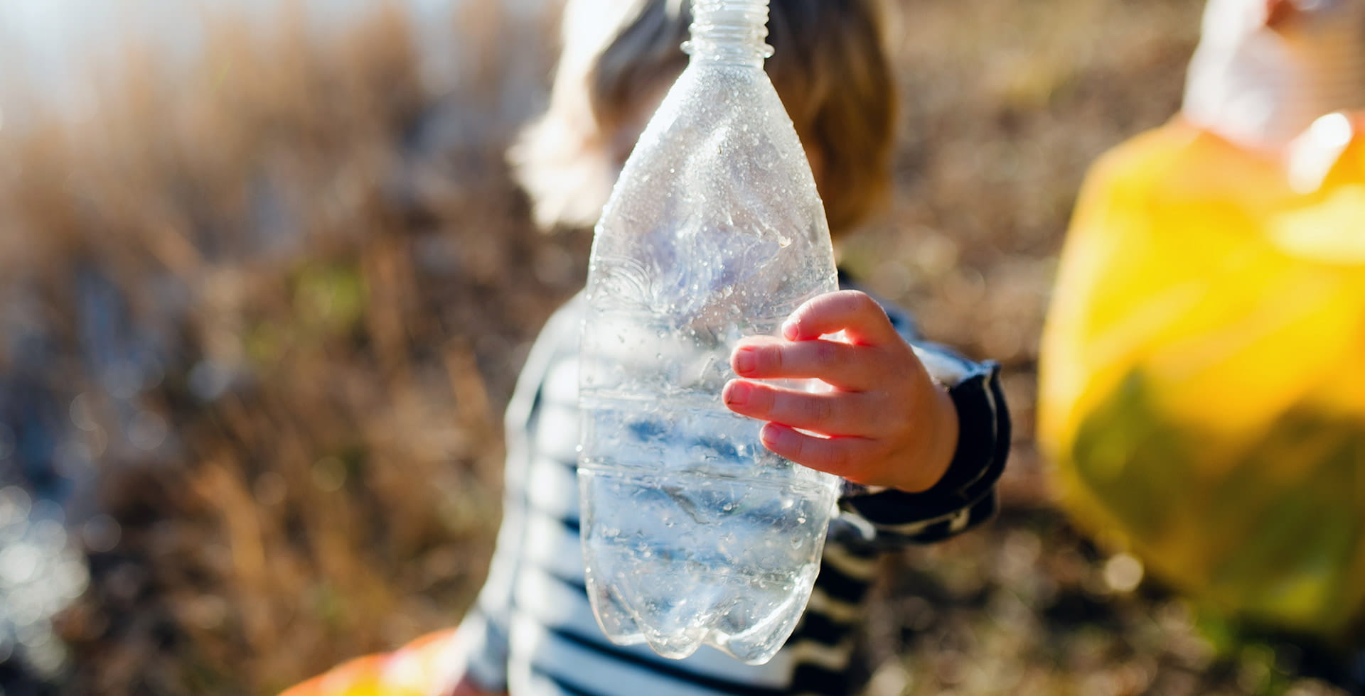 Enfant tenant une bouteille en plastique à la lumière du soleil – Libérer le potentiel des emballages durables